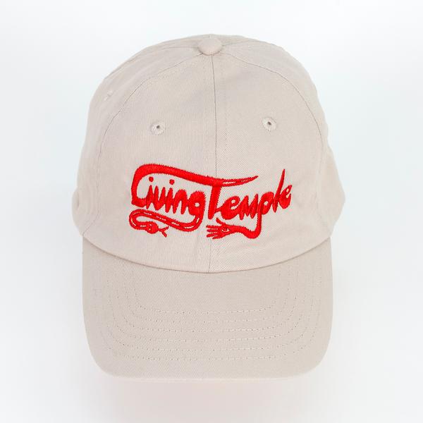 A photograph of a tan baseball cap with scripted text reading "Living Temple" embroidered on the front in red thread