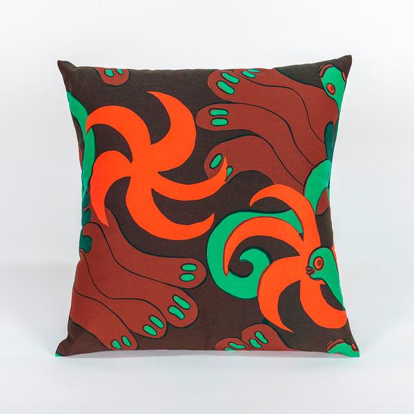 A square pillow made of fabric featuring a repeating textile pattern with stylized green snakes intertwined with abstract brown shapes and bright orange spirals on a dark brown background.