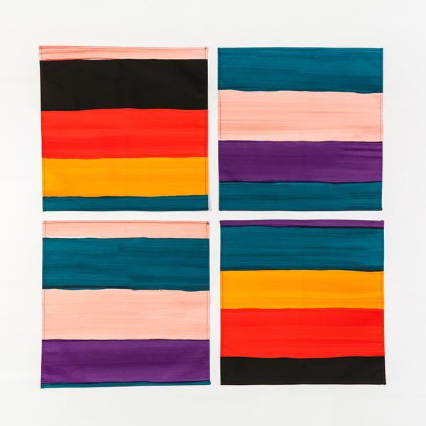 A set of four napkins made of varying stripes of black, red, yellow, blue-green, peach, and purple.