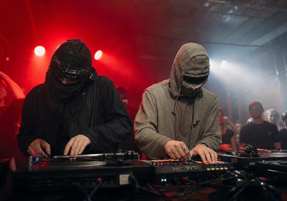 Anonymous breakbeat DJ duo performing in a red-lit underground club