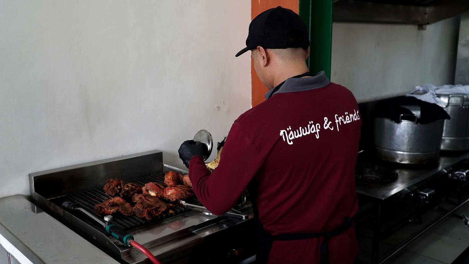 Kru Nawwaf & Friends memanggang potongan daging di atas grill di dapur restoran