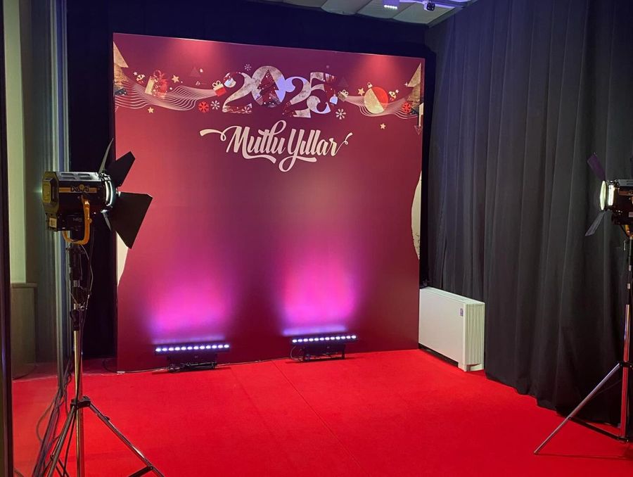 Photo backdrop reading "2025 Mutlu Yıllar" on a red carpet, lit by pink uplights and a studio spotlight, at Tüpraş's new-year celebration - BACKSTAGE Event production