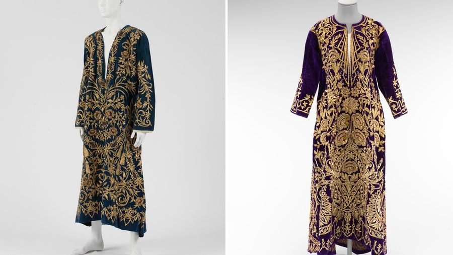 Two velvet dresses embroidered with gold thread on display stands, one dark blue and one purple