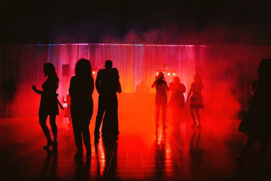 Silhouettes of guests dancing on a floor lit in deep red, with haze in the air