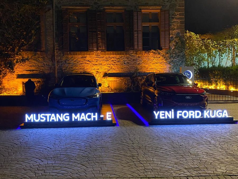 The same launch after dark — illuminated model lettering and façade uplighting carry the reveal