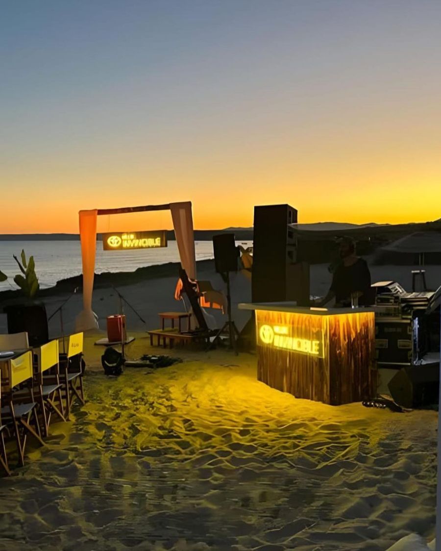 Beleuchtete DJ-Bühne mit Line-Array-Lautsprechern auf dem Sand bei Sonnenuntergang — BACKSTAGE Event Produktion für ein Strandevent an der türkischen Küste
