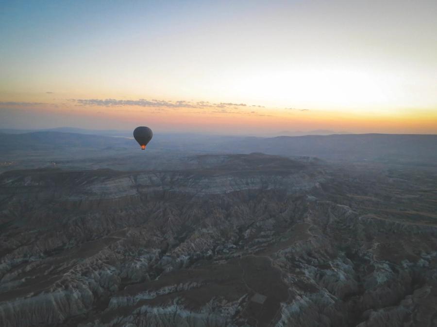 A single hot air balloon over the valleys of Cappadocia at first light, with the burner lit