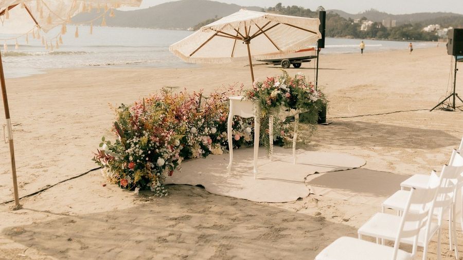 Aufbau einer Strandzeremonie: über den Sand gelegte Matten, weiße Stühle, eine Blumeninstallation und ein Lautsprecherstativ
