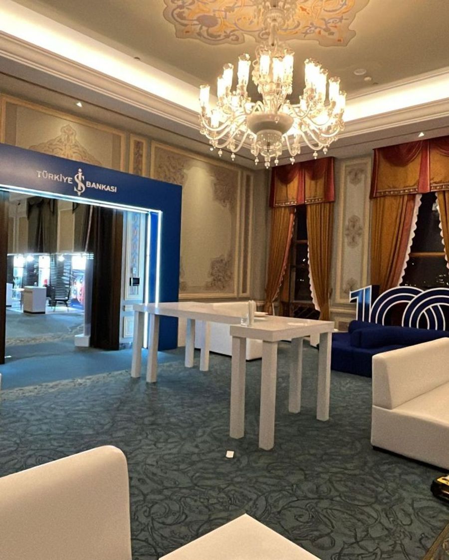 Historic palace hall with a chandelier, a blue branded entrance portal and white standing tables, set up for İş Bankası's 100th anniversary - BACKSTAGE Event production