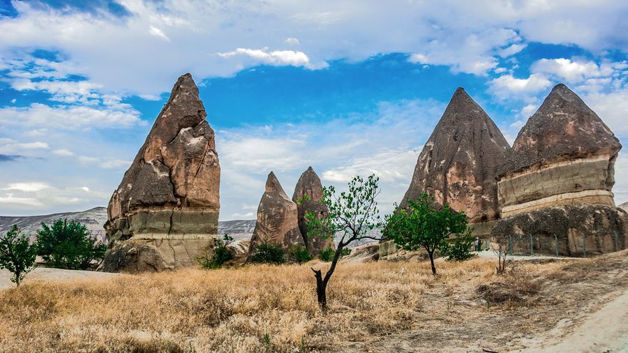 Cone-shaped fairy chimneys among dry grass in Cappadocia under a cloudy blue sky