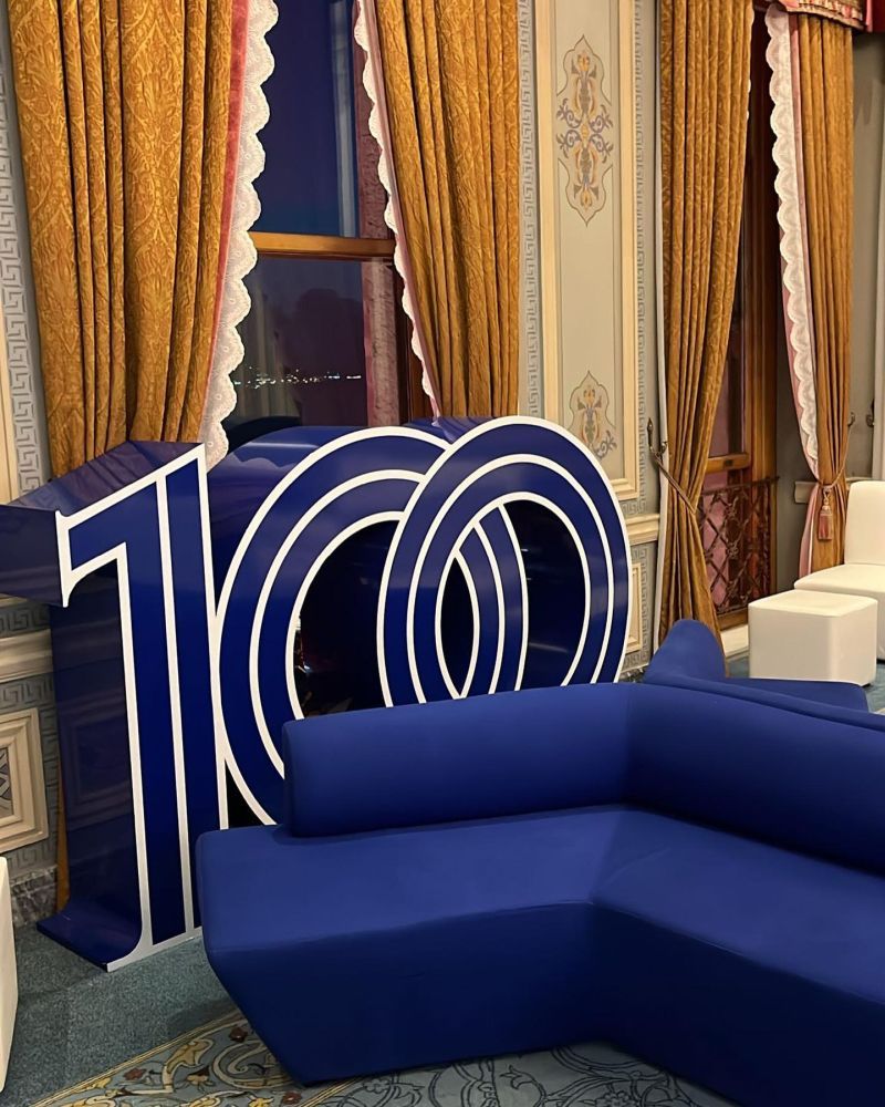 Three-dimensional "100" installation and blue lounge sofas in a heritage hall with gold curtains, built for İş Bankası's 100th anniversary - BACKSTAGE Event production
