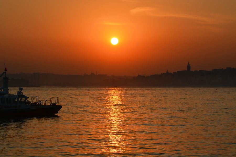 Sunset over the water in Istanbul, with Galata Tower and the skyline in silhouette and a boat in the foreground