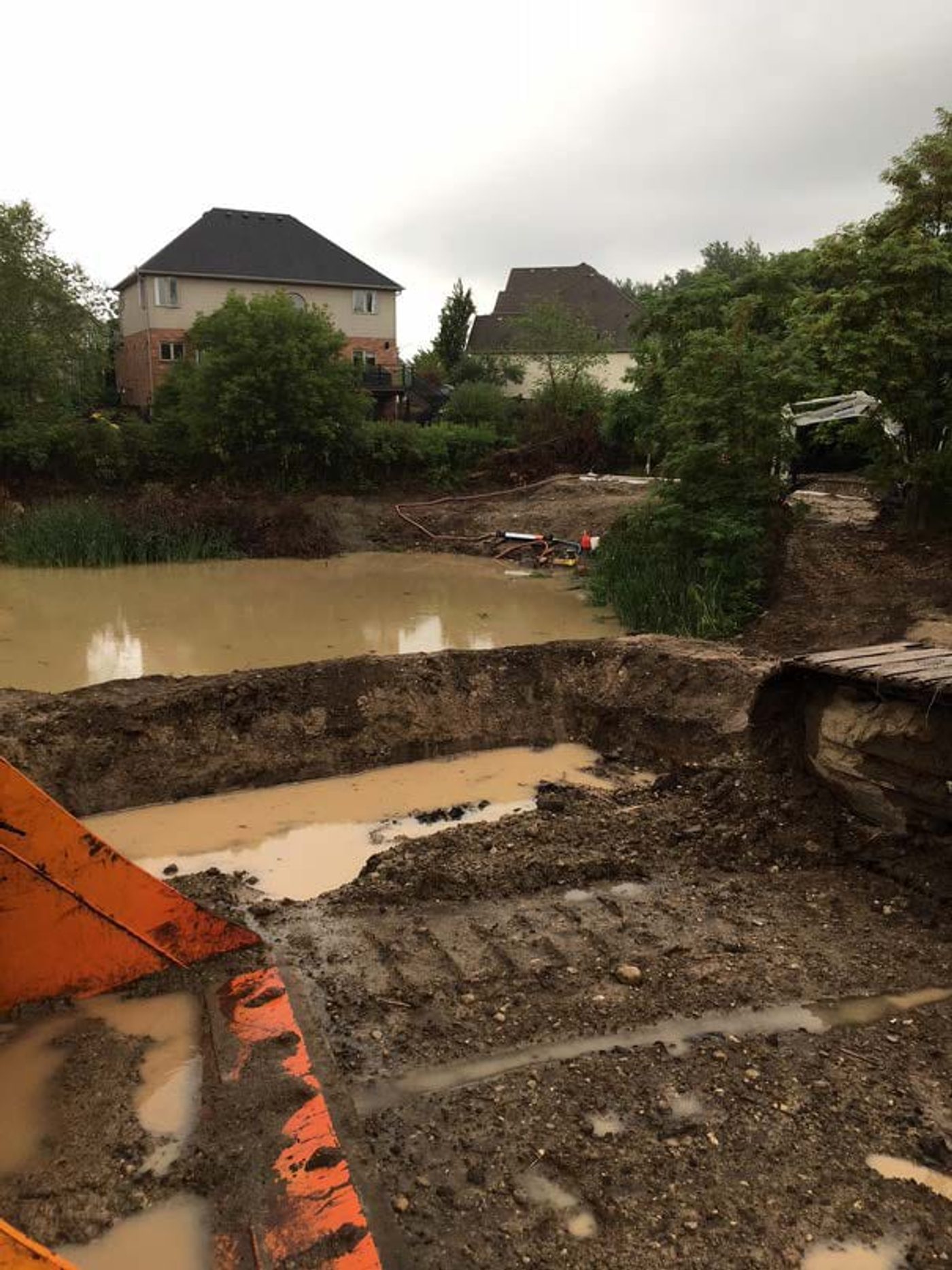 Pond 53 seen from the bank with an excavator arm in the foreground and houses behind
