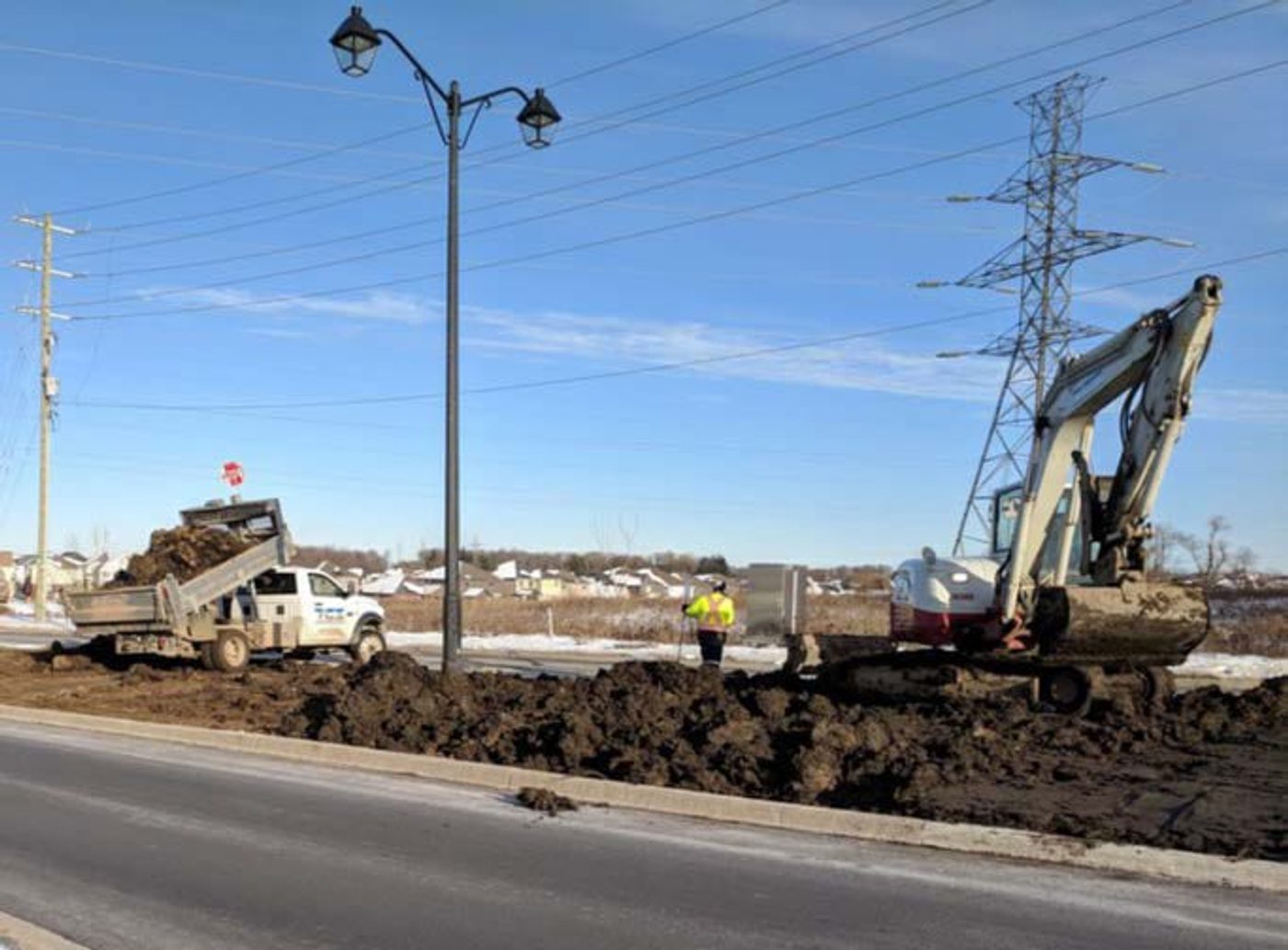 Truck and excavator spreading amended sediment along a municipal boulevard