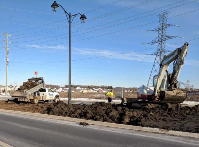 Truck and excavator spreading amended sediment along a municipal boulevard