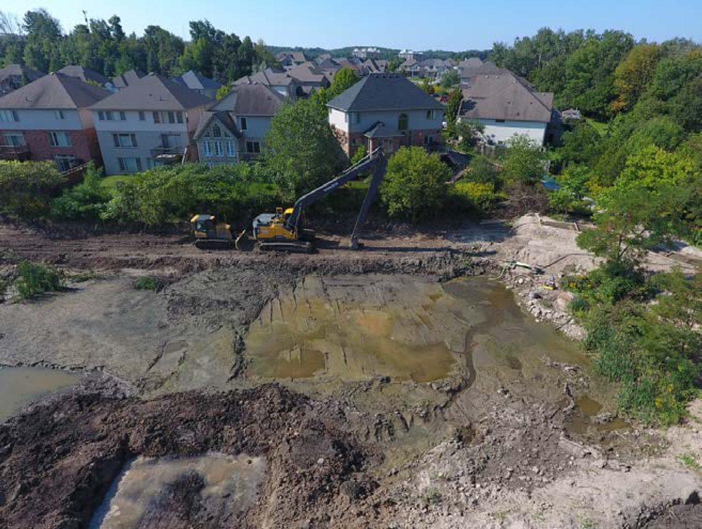Aerial view of Pond 53 at capacity with an excavator working the sediment beside backyards