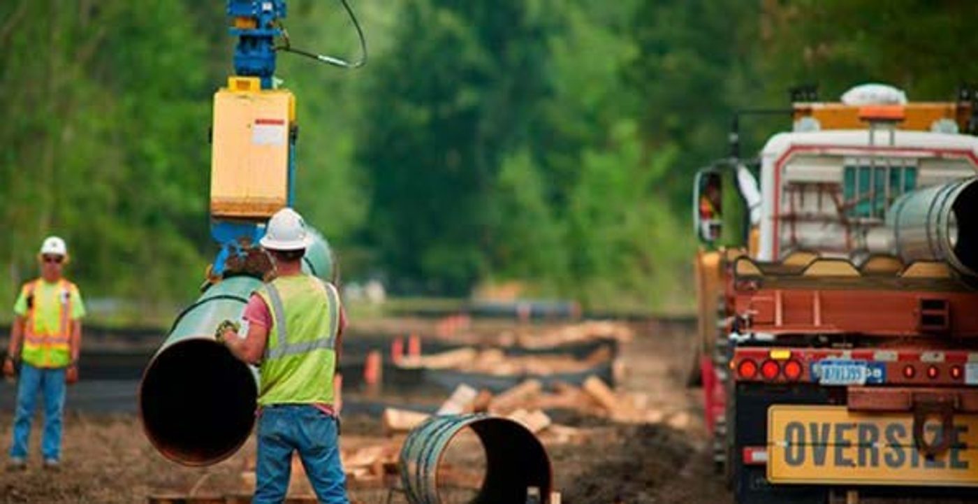 Crew working on pipeline sections beside an oversize load truck