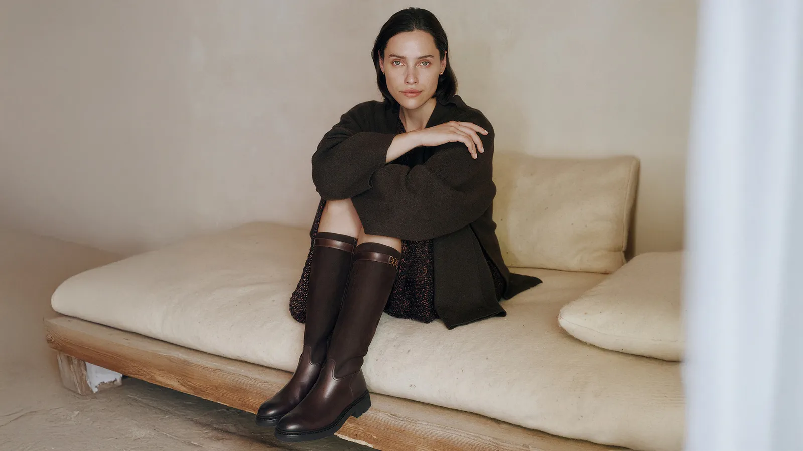 Dame i mørke klær sittende på en seng