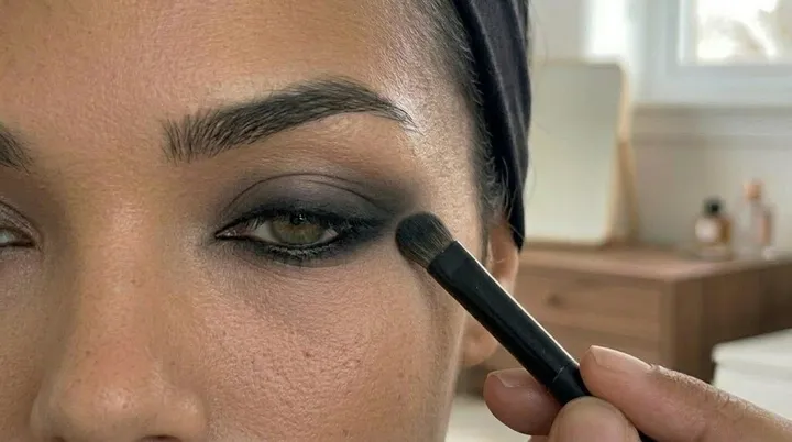 Makeup brush blending black kohl eyeliner into a soft smokey effect for a dark feminine eye makeup tutorial.