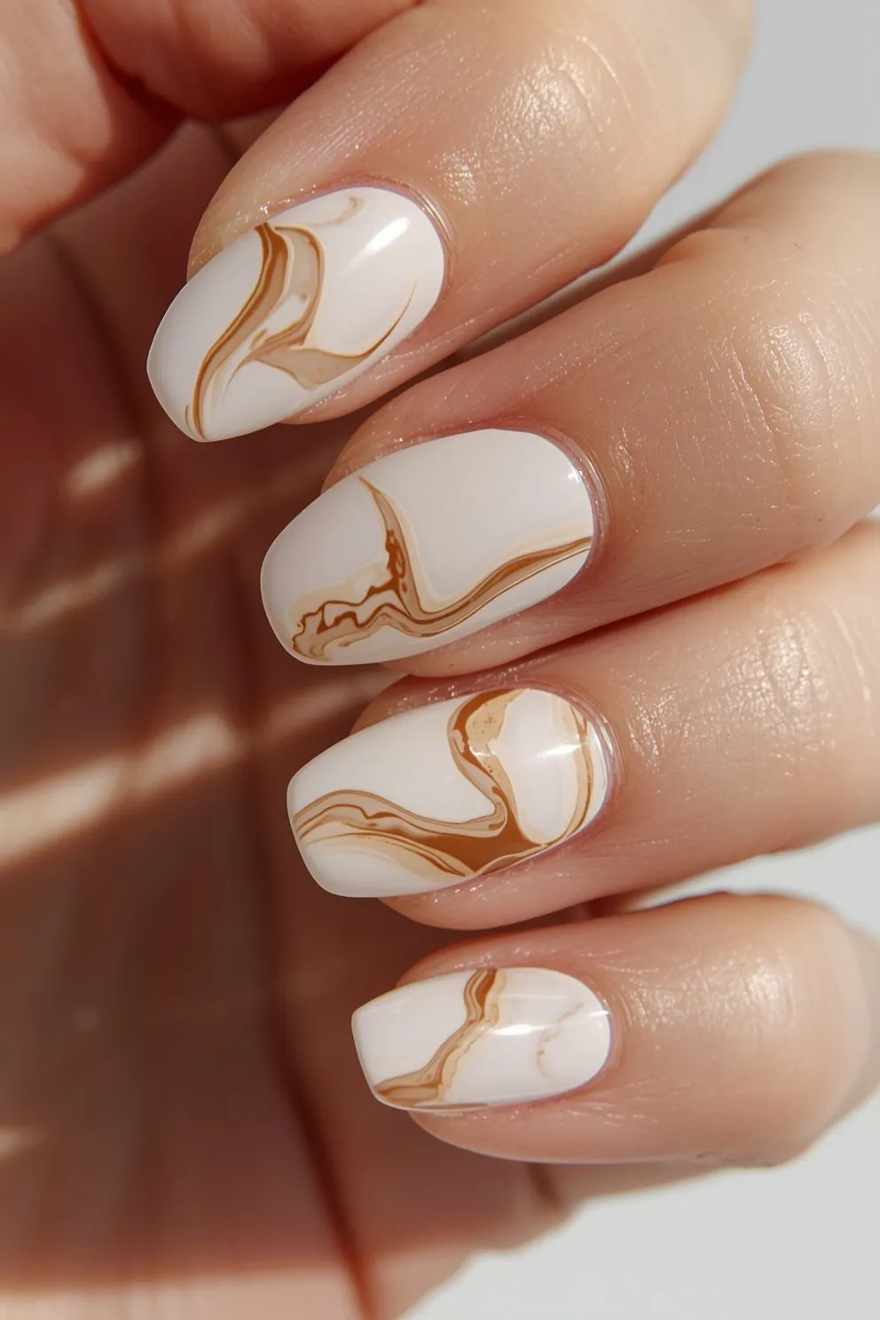 Neutral nude nails with soft caramel swirl patterns, glossy almond shape nails inspired by coffee tones and minimal summer nail trends