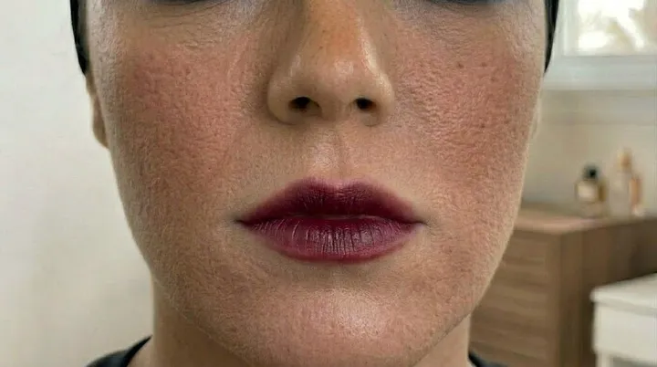 Makeup brush softly blending the edges of dark berry lipstick to create a diffused romantic lip effect.