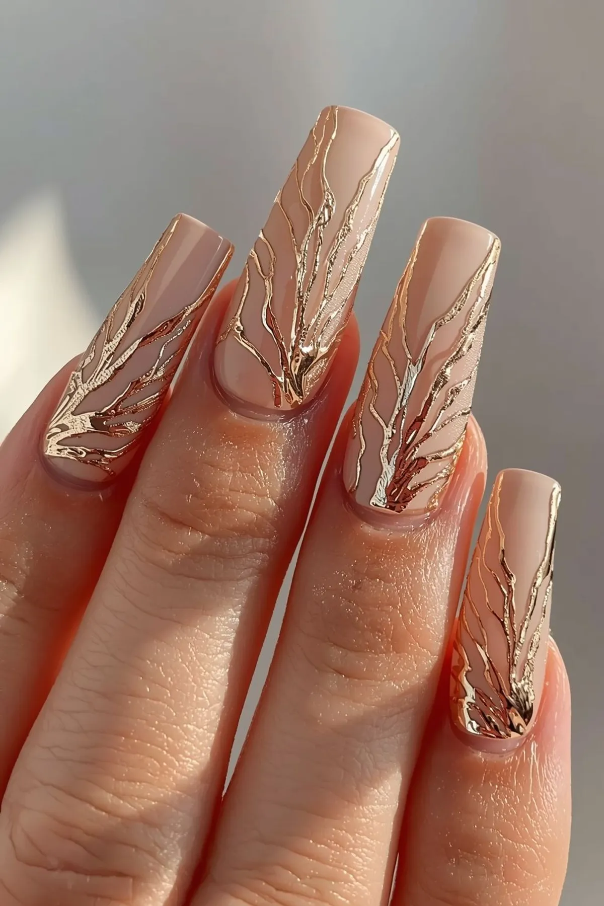 Elegant nude almond-shaped nails with flowing metallic gold vein detailing, glossy finish, and luxury minimal nail art aesthetic