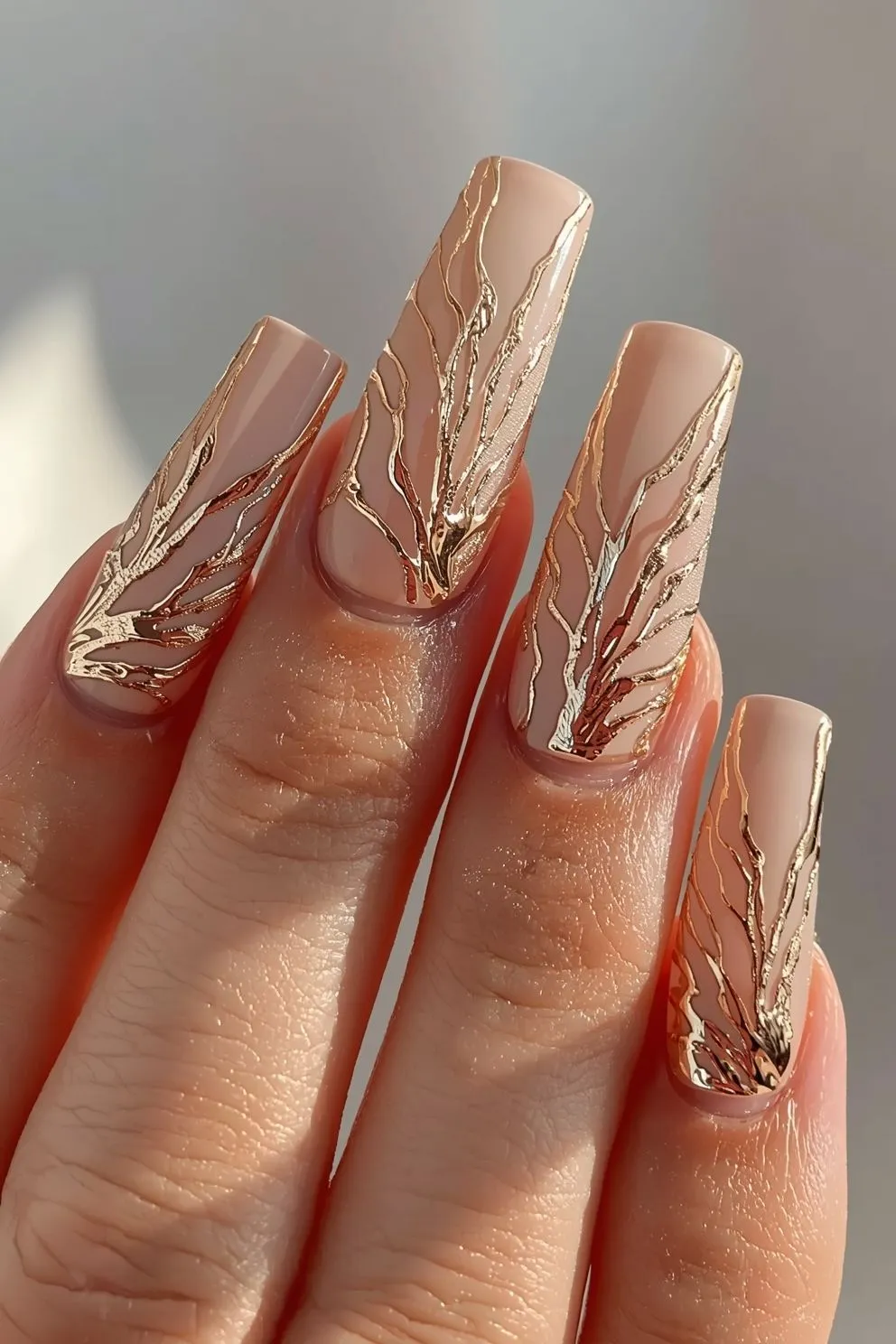 Elegant nude almond-shaped nails with flowing metallic gold vein detailing, glossy finish, and luxury minimal nail art aesthetic