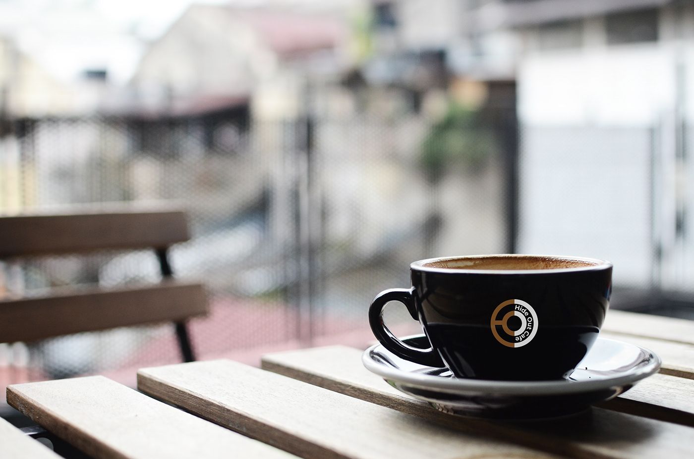 Black coffee cup with the Hide Out Cafe logo on a wooden table