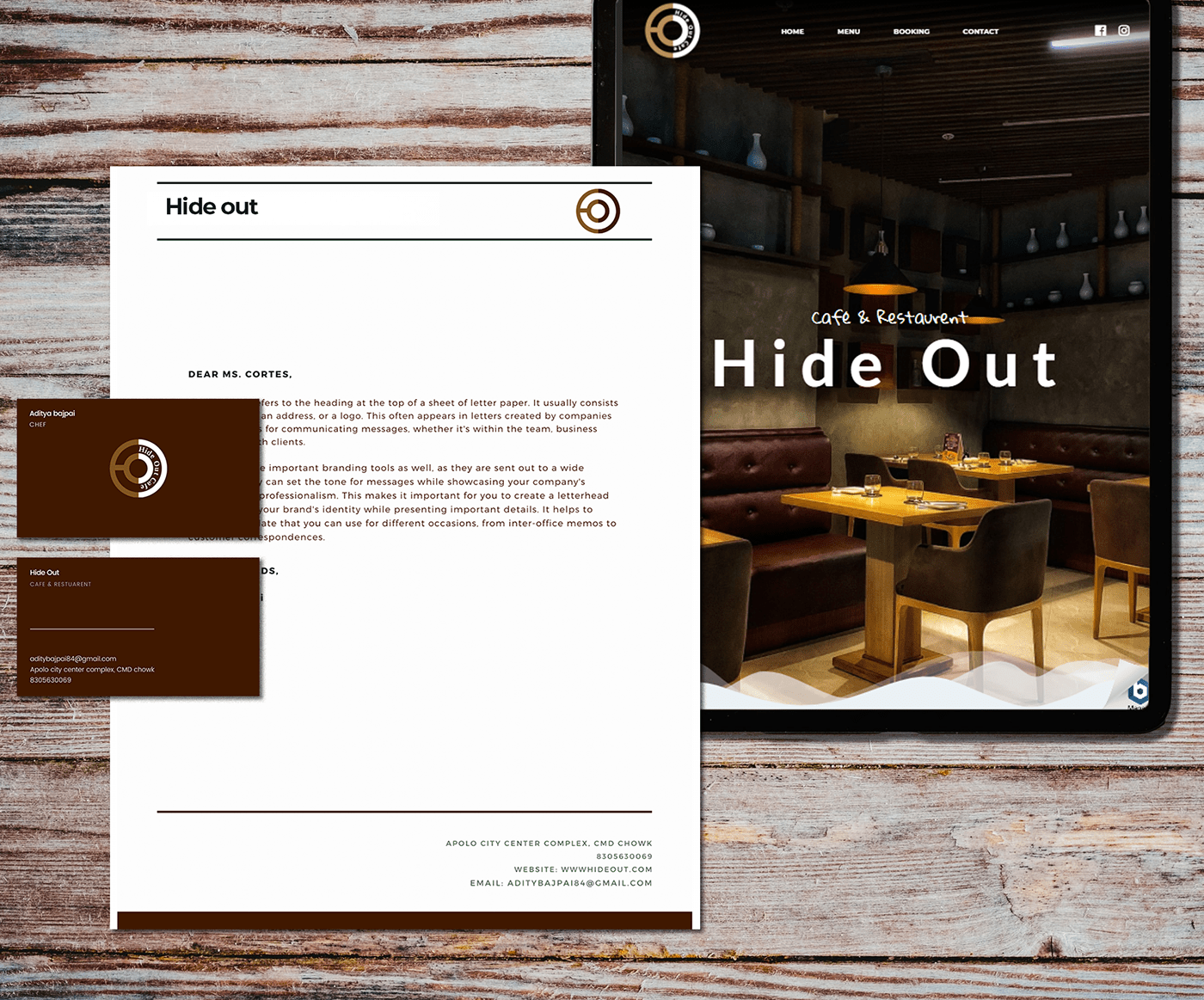Hide Out Cafe letterhead and brown business cards beside a website on a tablet, on weathered wood
