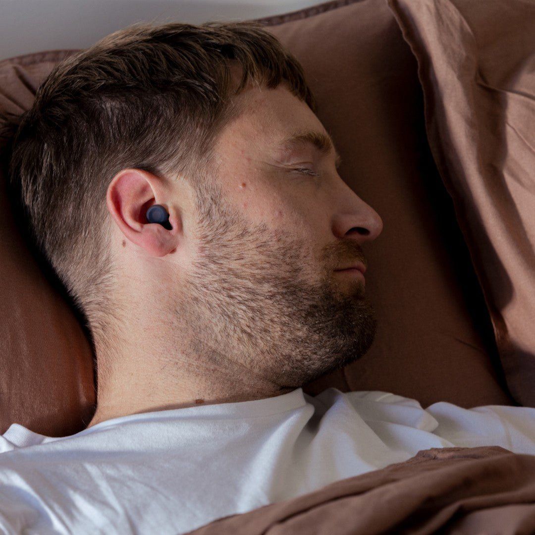 Man asleep on a pillow with a black Loop Dream earplug in his ear