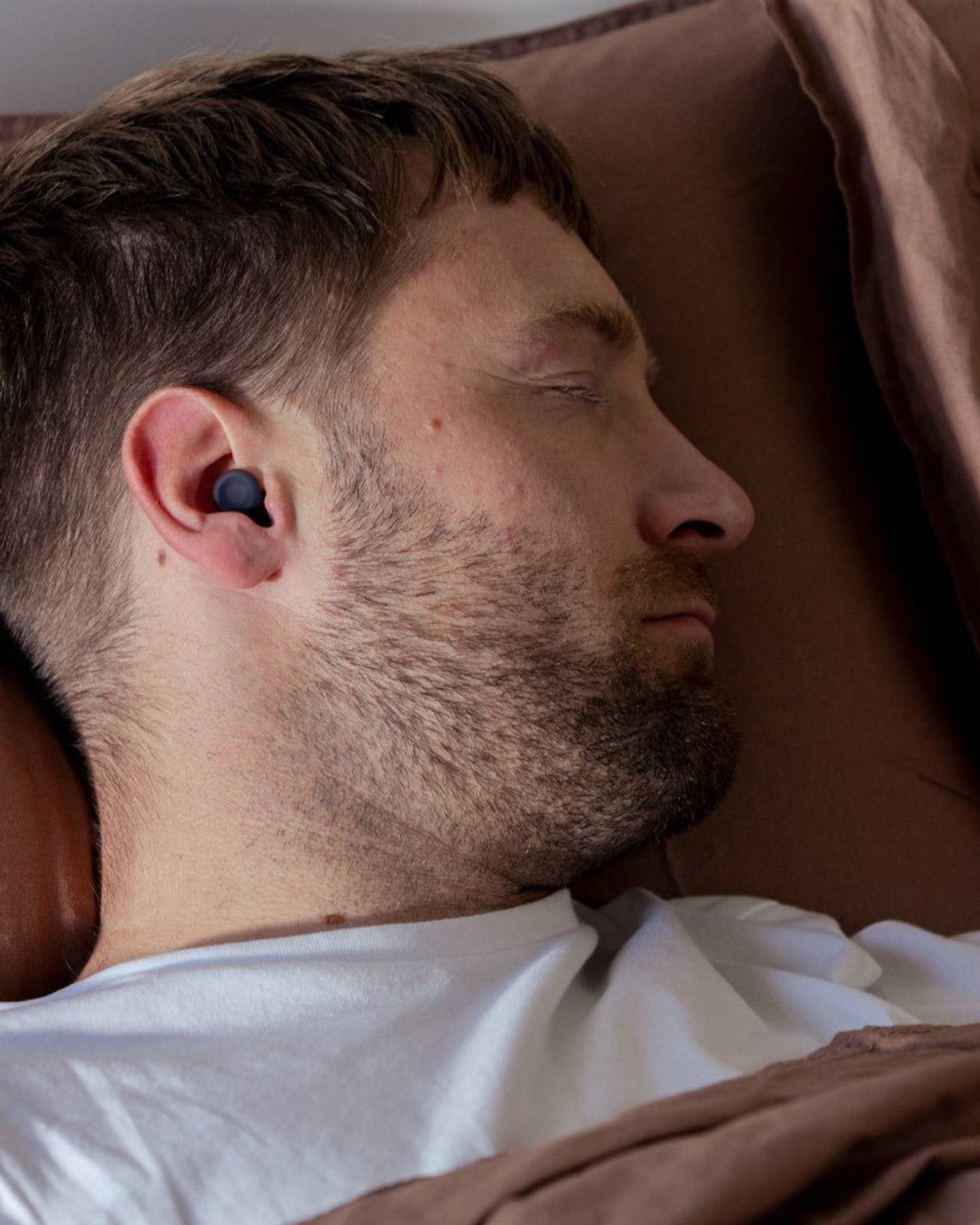 Man asleep on a pillow with a black Loop Dream earplug in his ear