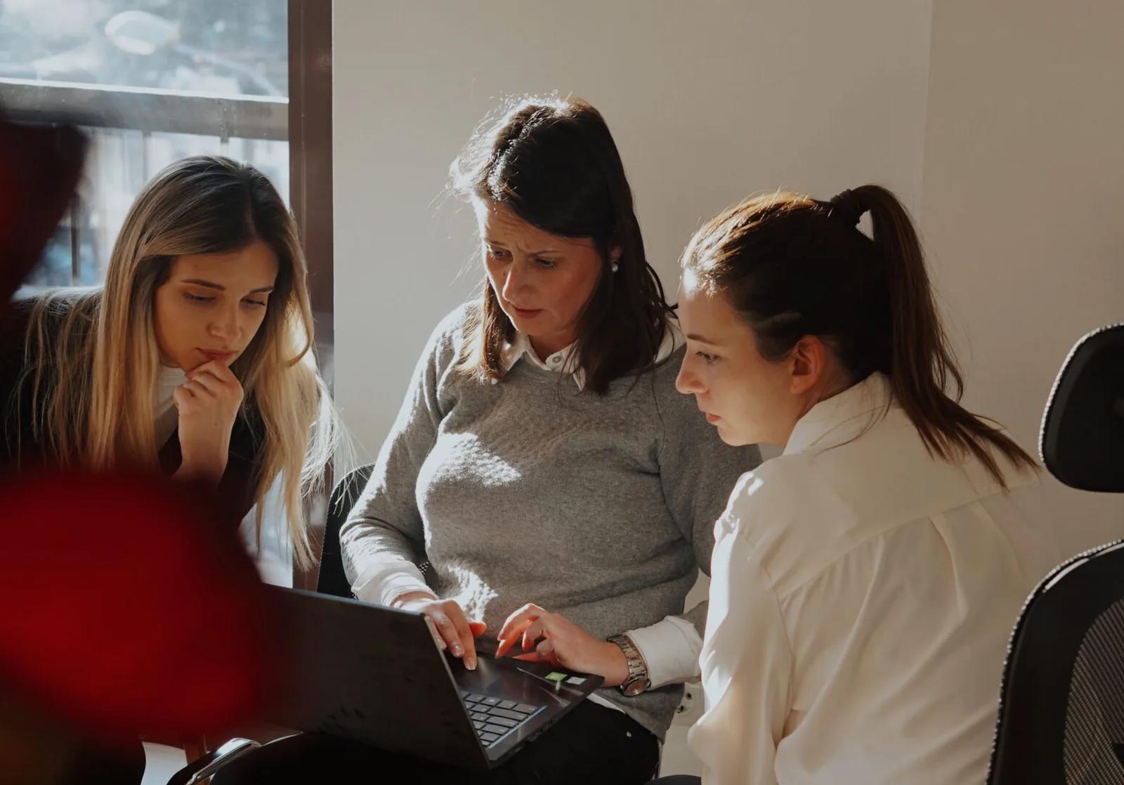 Drie collega's overleggen samen achter een laptop bij het raam