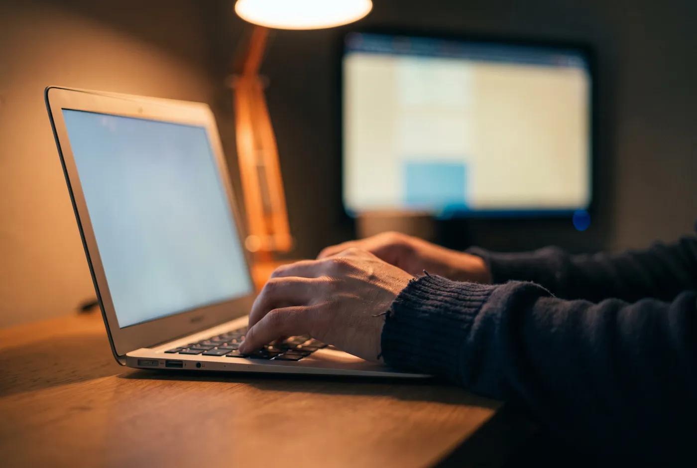 Handen typen op een laptop bij warm bureaulamplicht, sourcing-sfeer