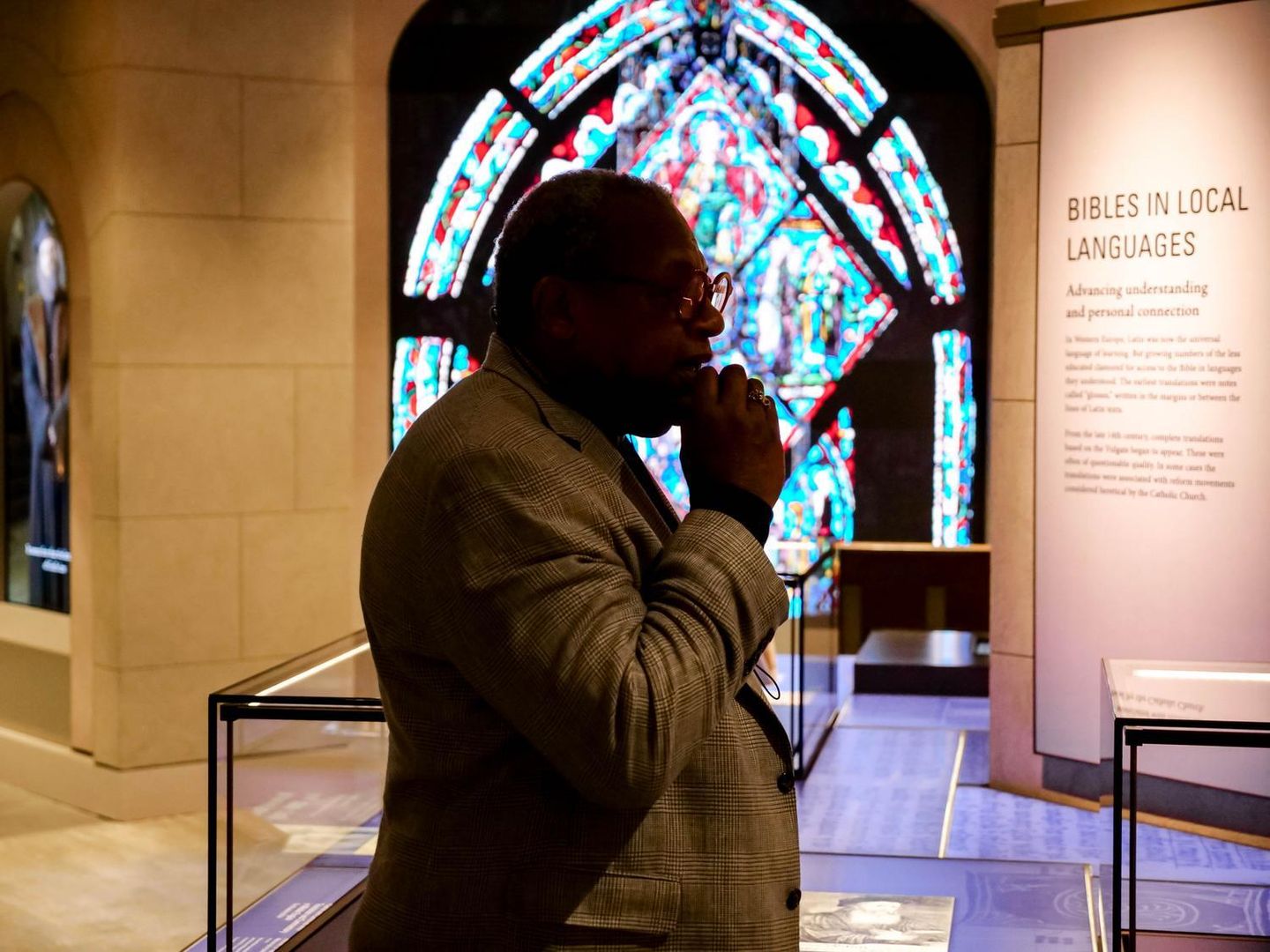An Inspire guide teaches guests about the global impact of Bible translation in the Museum of the Bible's "Bibles in Local Languages" exhibit, with a stained-glass display in the background.