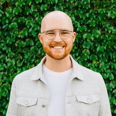 A smiling man wearing glasses stands in front of green ivy