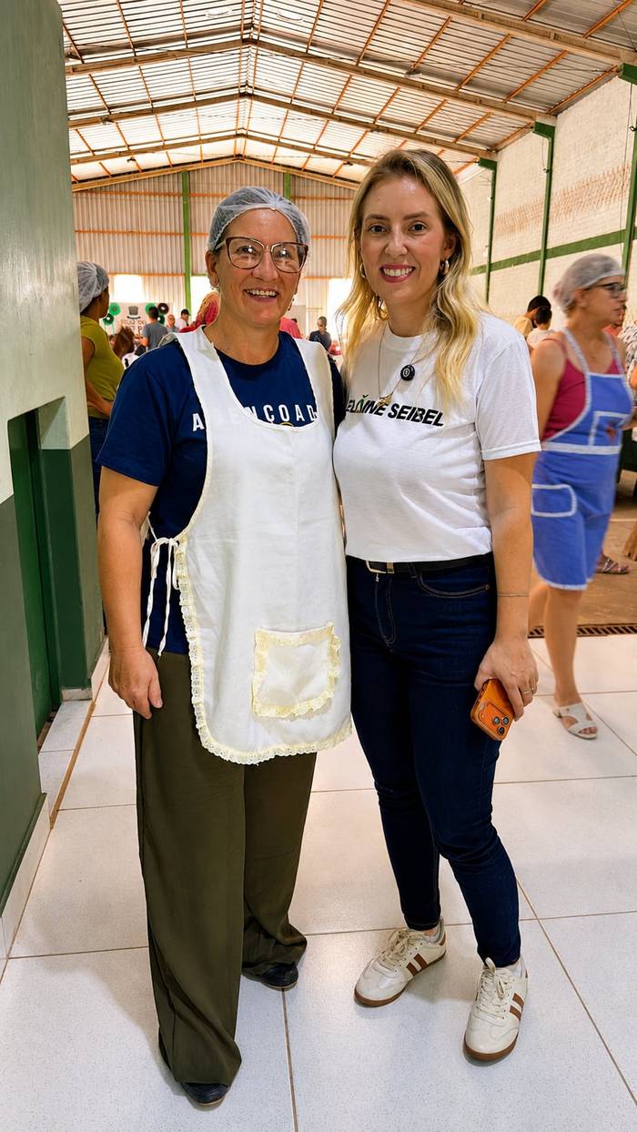 Elaine ao lado de mulheres de avental que preparam um evento comunitário.