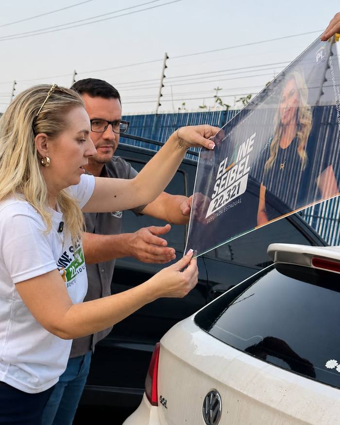 Elaine e um apoiador aplicando o adesivo perfurado no vidro traseiro de um carro.