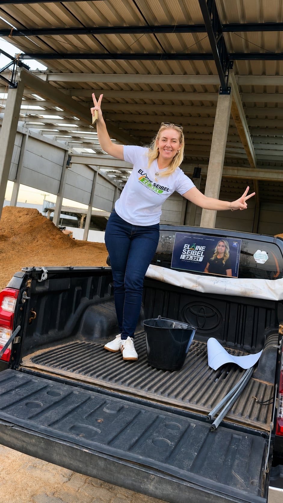 Elaine na caçamba de uma caminhonete com o adesivo da campanha no vidro, num galpão do agro.