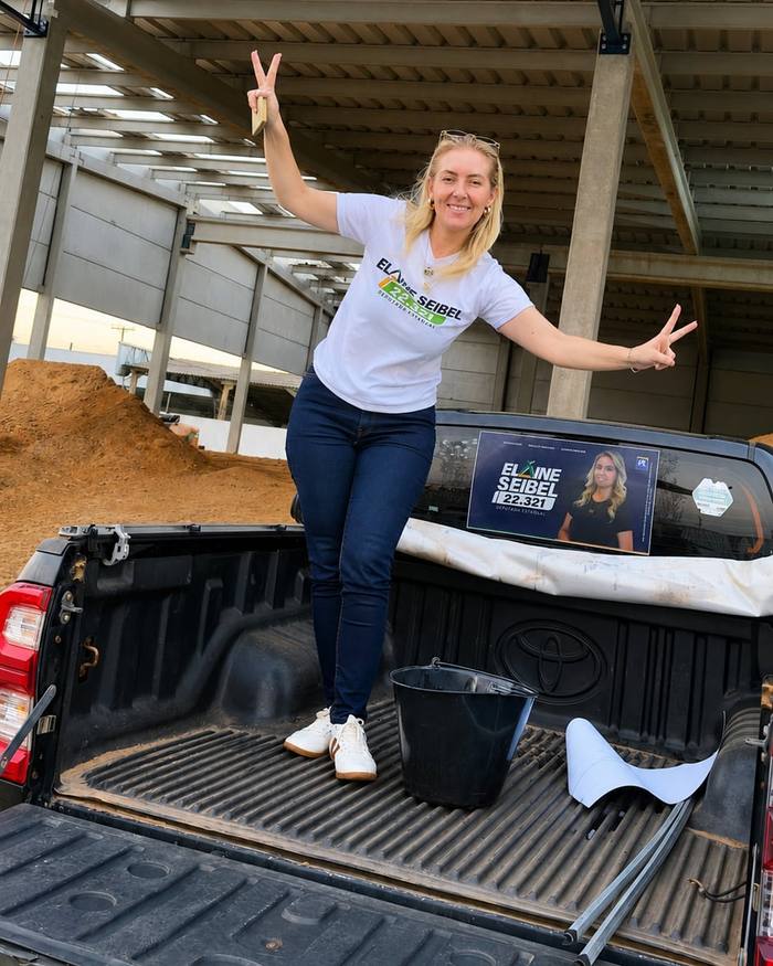 Elaine na caçamba de uma caminhonete com o adesivo da campanha no vidro, num galpão do agro.