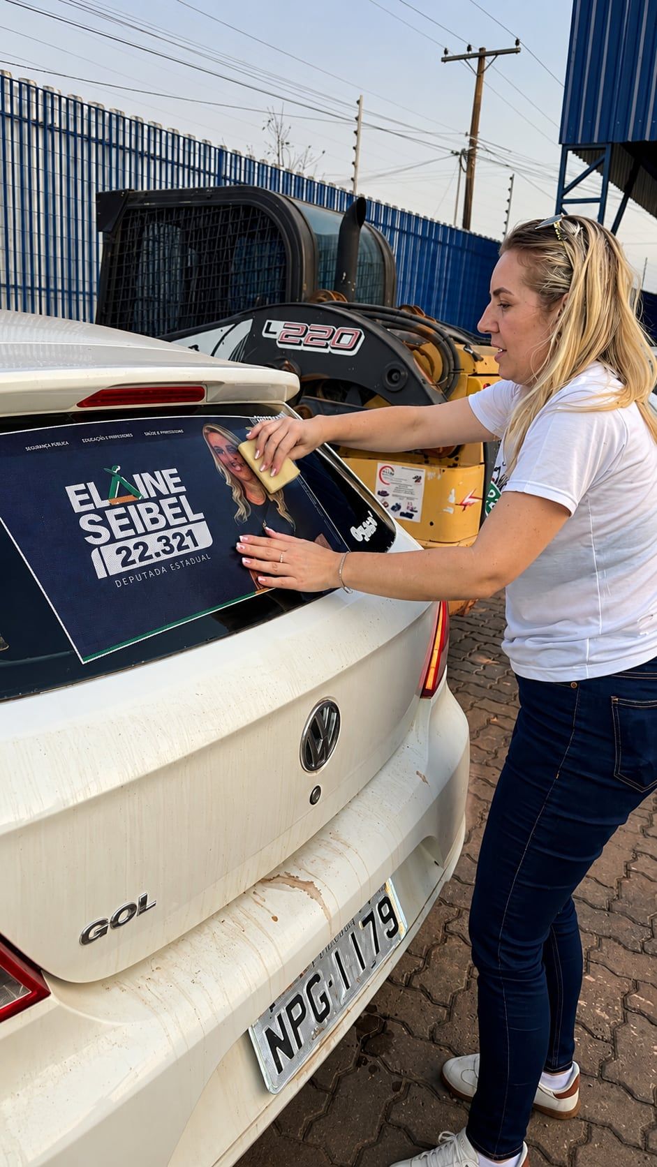 Adesivo da campanha sendo aplicado no vidro traseiro de um carro branco.