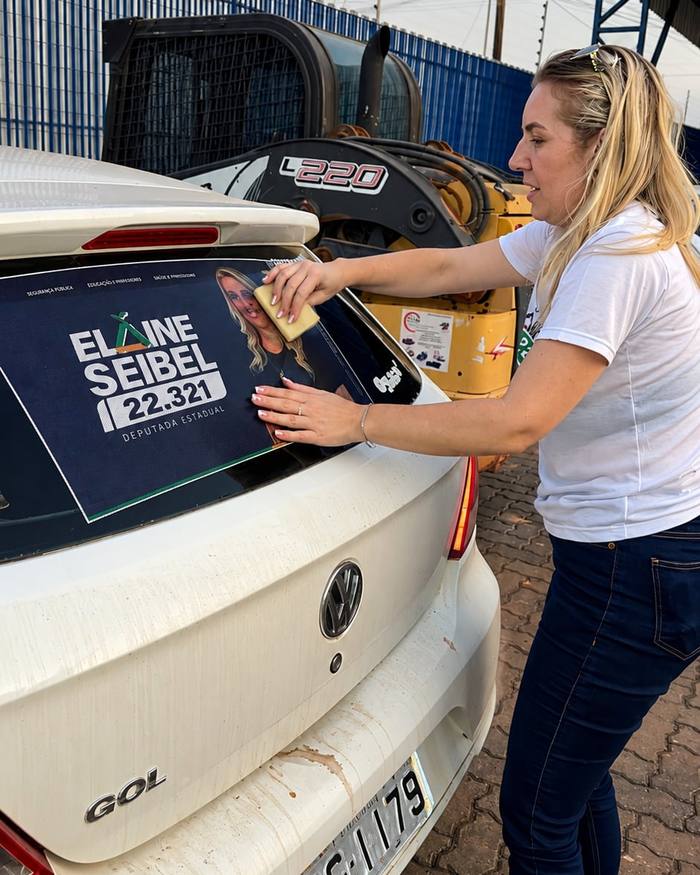 Adesivo da campanha sendo aplicado no vidro traseiro de um carro branco.