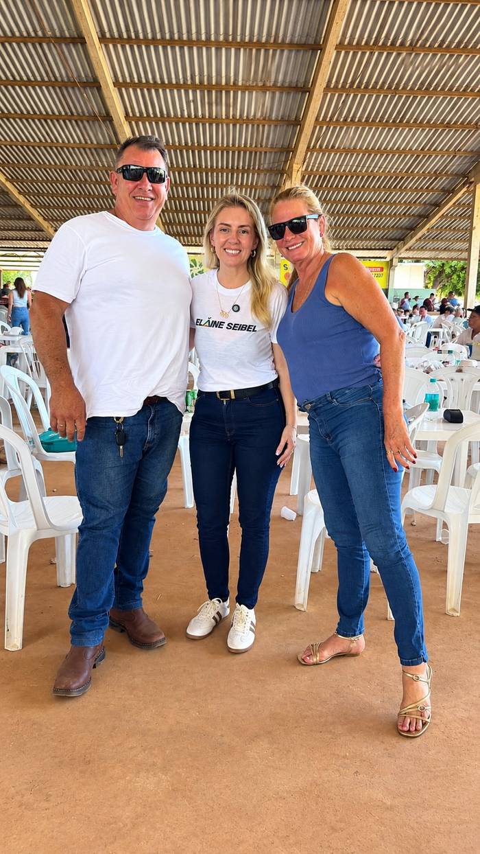 Elaine entre dois apoiadores num encontro de campanha sob uma tenda.