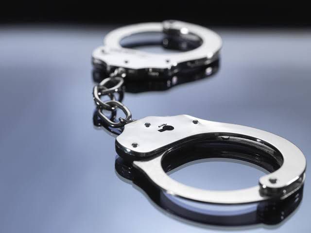A pair of open metal handcuffs linked by a chain, resting on a reflective grey surface