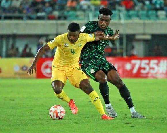 Footballer in yellow shields the ball from an opponent in green during a night match
