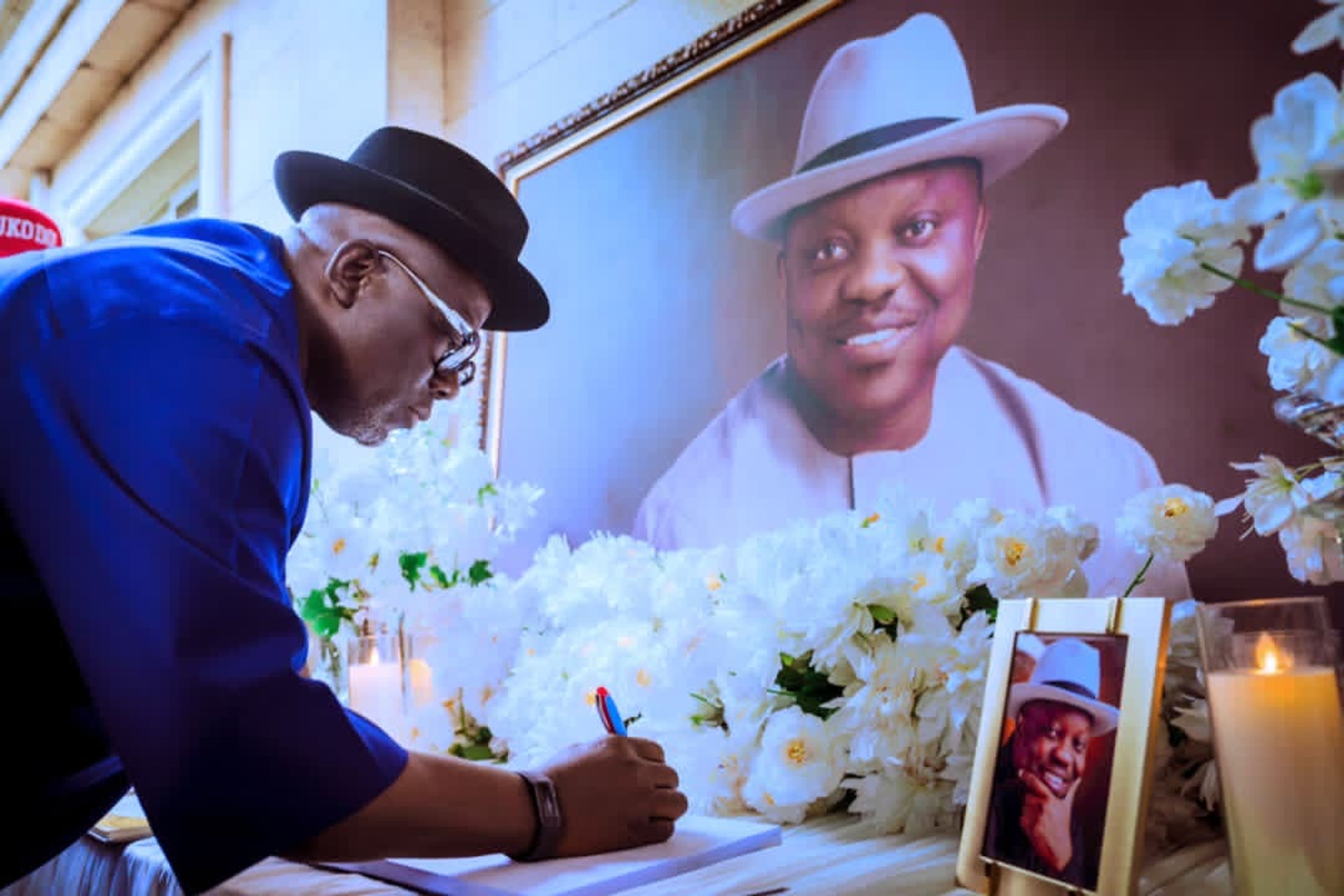 Sheriff Oborevwori in a blue attire, bent over a desk with the picture of the late Emmanuel Eweta Uduaghan, signing a memorial book. 