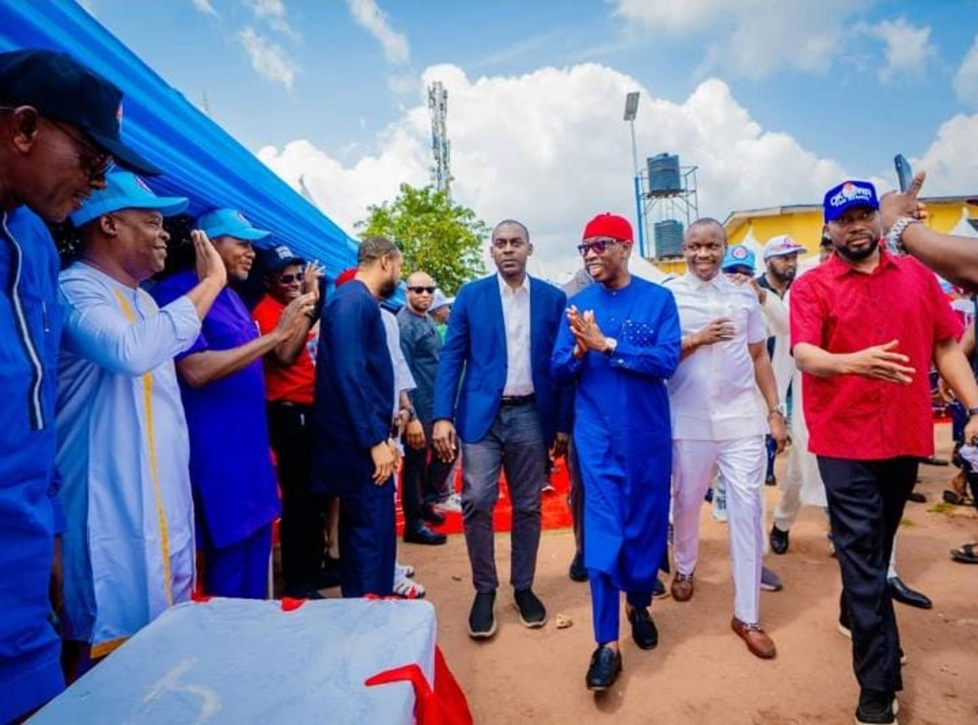 Ifeanyi Okowa dressed in Nigerian native attire and a red cap, walking amongst a group of men behind him