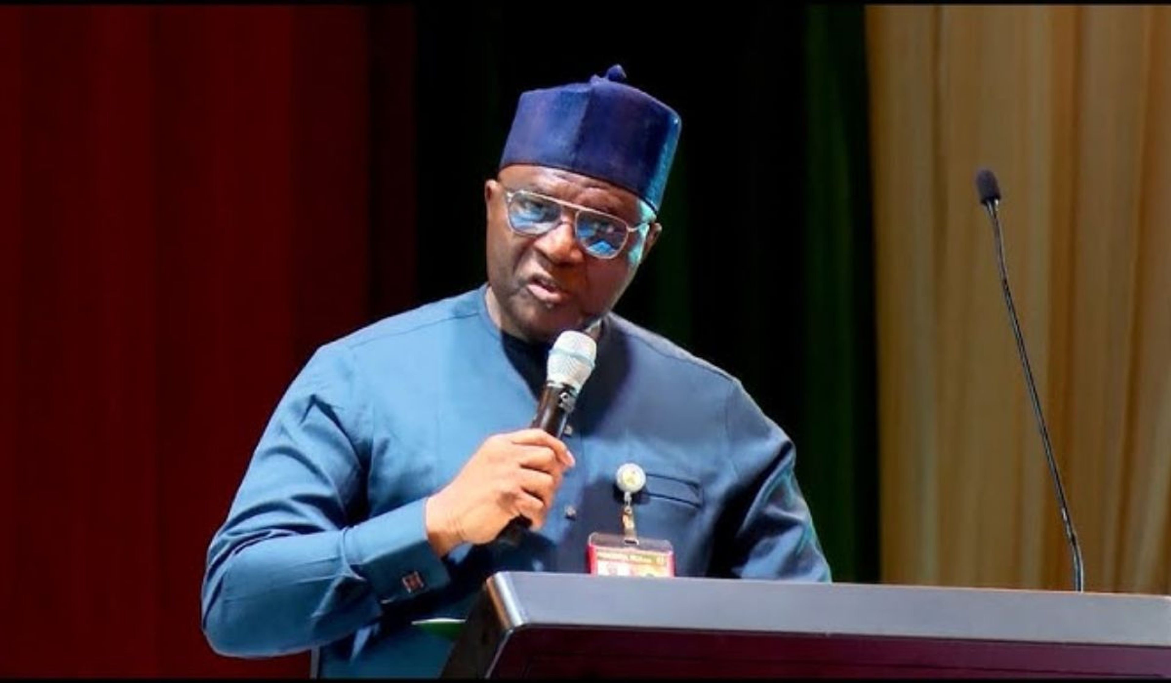 Medium shot of Bayo Onanuga wearing a blue traditional Agbada and matching cap while addressing an audience 