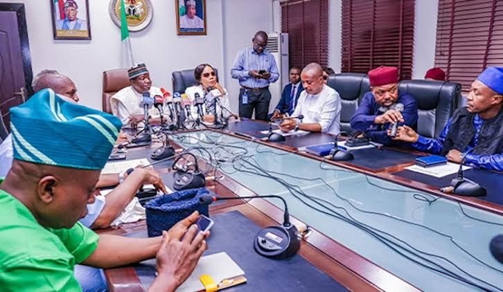 Officials and union leaders seated around a conference table with microphones during a meeting in a government boardroom
