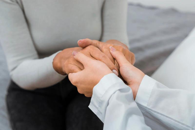 Primer plano de unas manos sosteniendo con delicadeza la mano de otra persona sentada en un sofá
