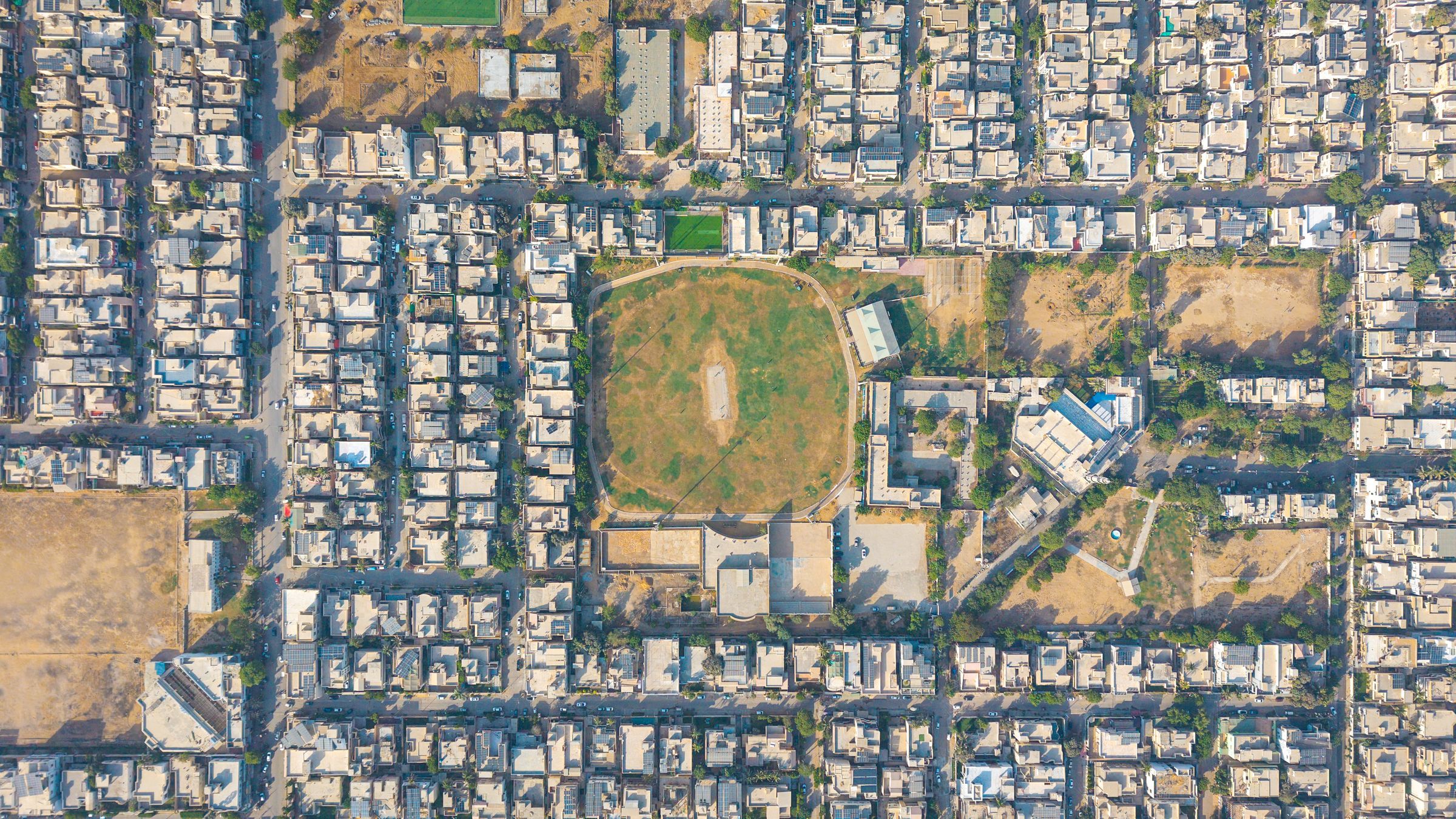 Top-down view of a dense Karachi neighbourhood with a cricket ground
